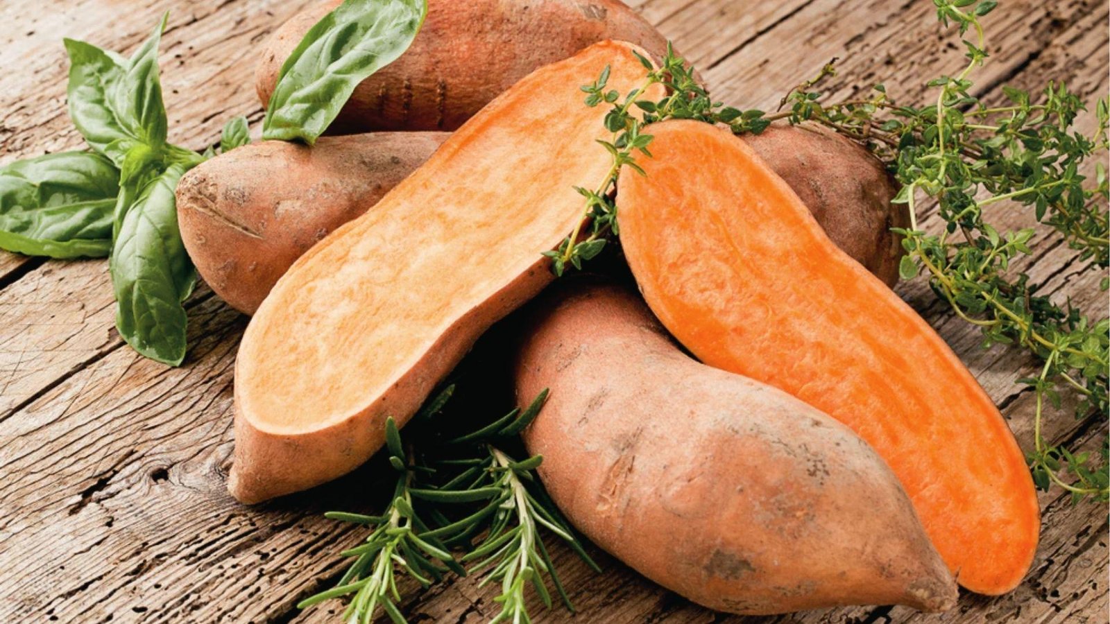 Fresh whole and sliced sweet potatoes with herbs on wood, rich in fiber and vitamins for dogs.