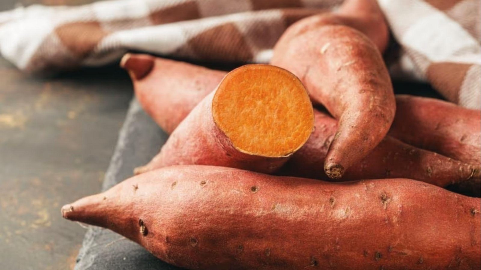 Raw sweet potatoes with one sliced open, showing orange flesh dogs can eat when cooked plain.